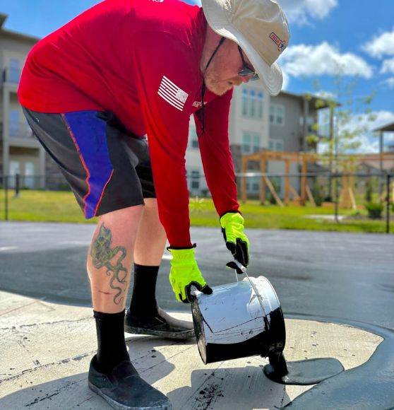 FIELD OPS employee pouring black paint on pickleball court